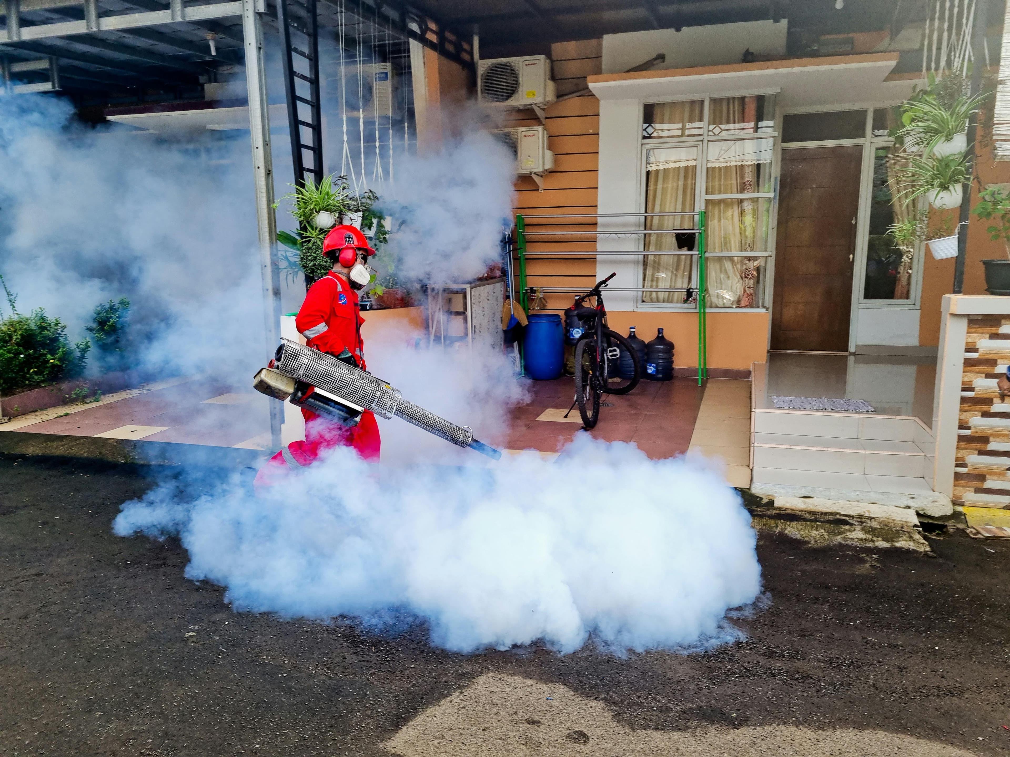 Pest control technician spraying treatment around a house